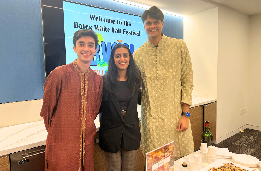 Two young men and one young woman smiling together in front of a "Diwali" themed table.