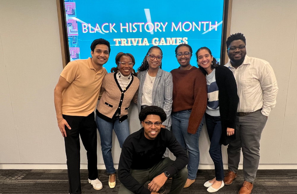 A group of young men and women grouped together and smiling. A screen behind them reads "Black History Month: Trivia Games."