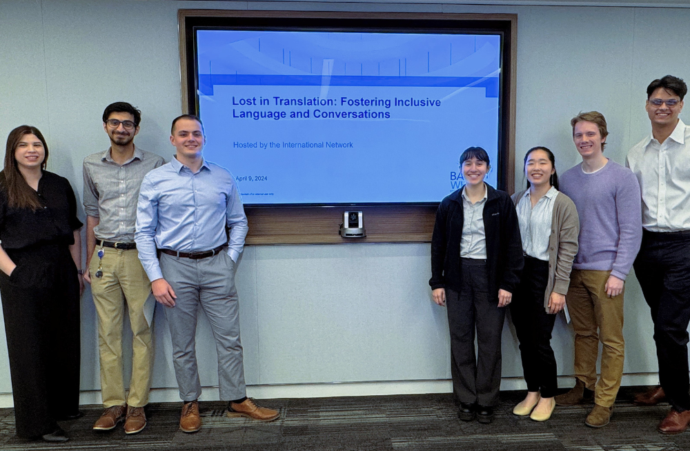 A group of employees smiling at the camera, standing around a screen that reads: "Lost in Translation: Fostering Inclusive Language and Conversations."
