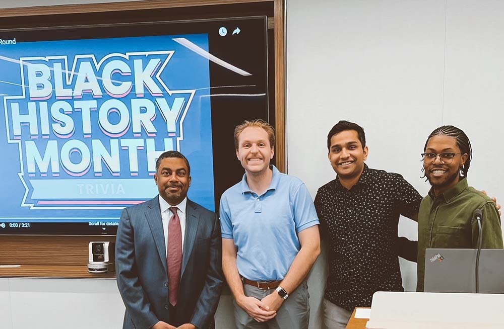 Four men smile at camera in front of sign that says Black History Month