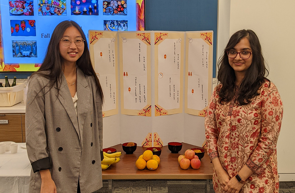 Two women standing next to table with fruit