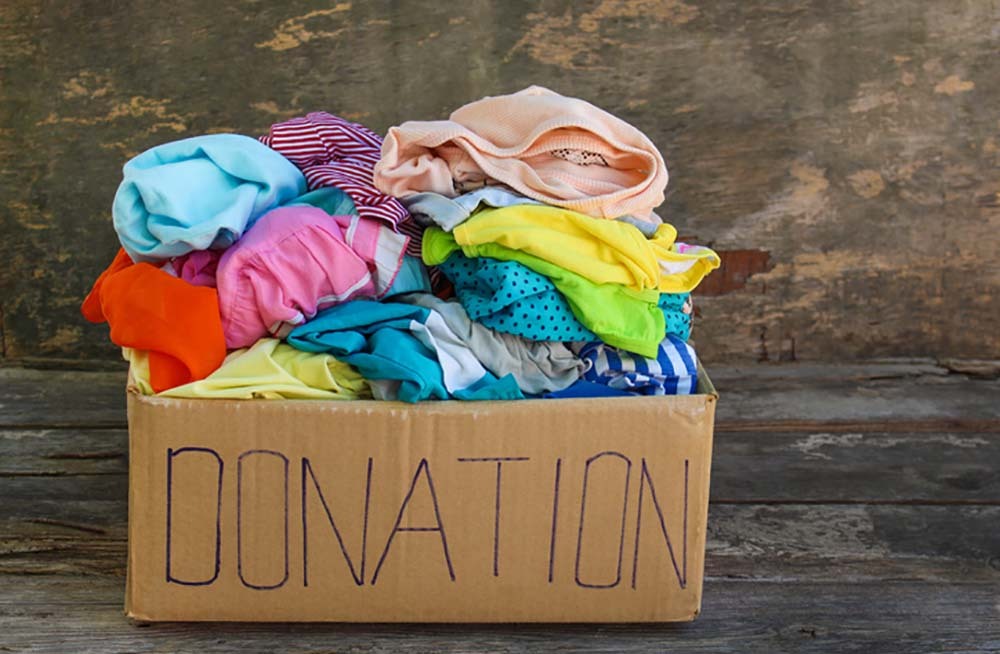 A cardboard box with Donations written on it is full of colorful, folded clothing