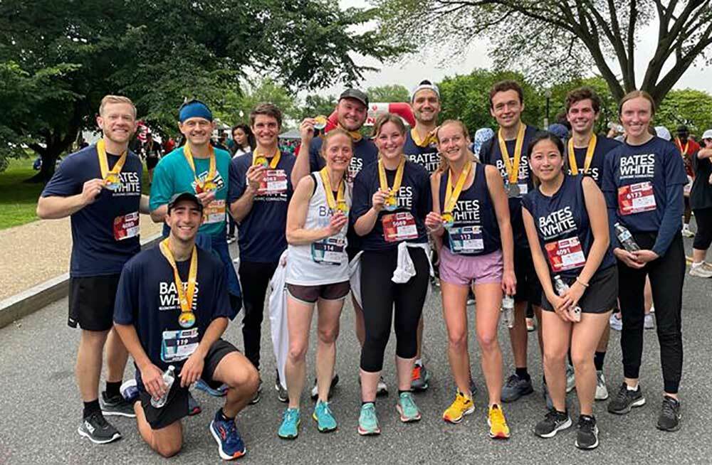 Group of people in shirts that say Bates White, wearing running shoes and raising medals around their necks, smile at the camera