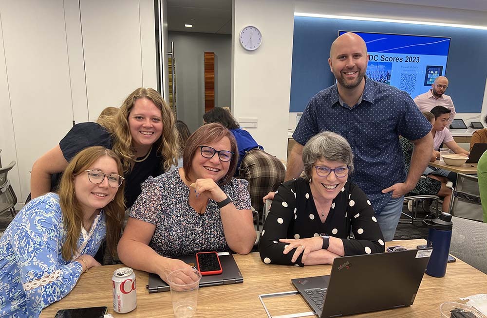 Group of colleagues sitting around computer smiling, playing Wordle.