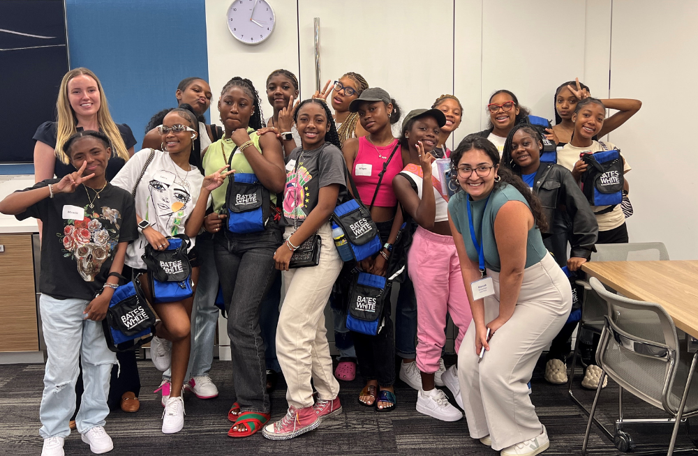 2 adult female employees with around a dozen teenage girls; they are clustered together, smiling, and some feature "peace" signs.