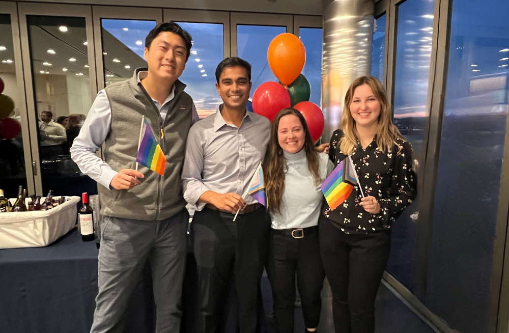 2 young men and 2 young women, standing together and smiling while holding rainbow flags.