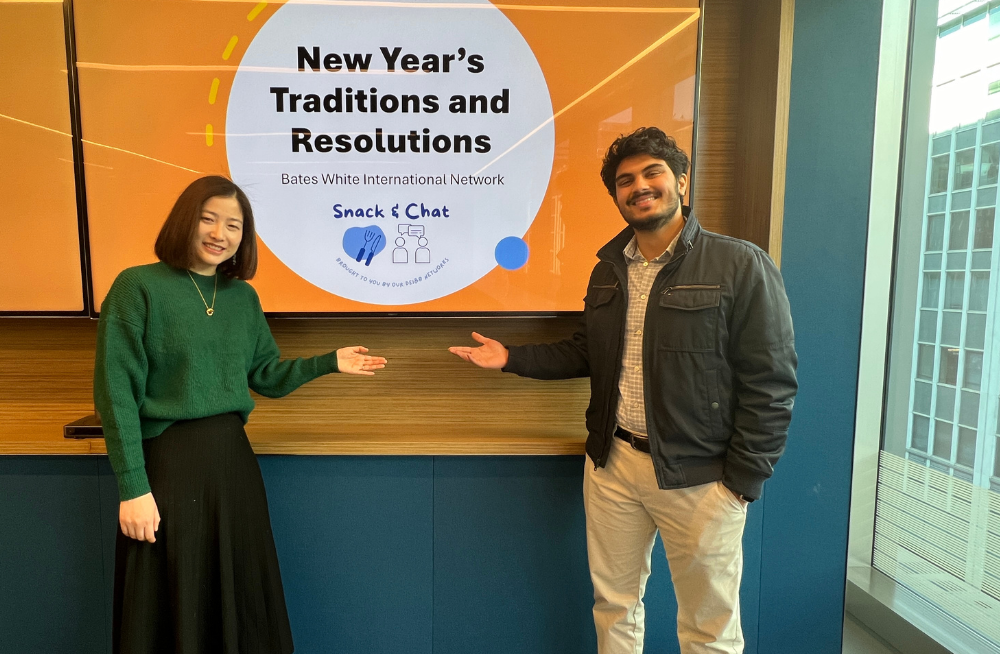 A young man and woman stand together, pointing at a screen behind them which reads, "New Year's Traditions and Resolutions."