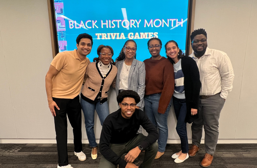 A group of smiling young men and women, standing together in front of a screen reading: "Black History Month Trivia Games."