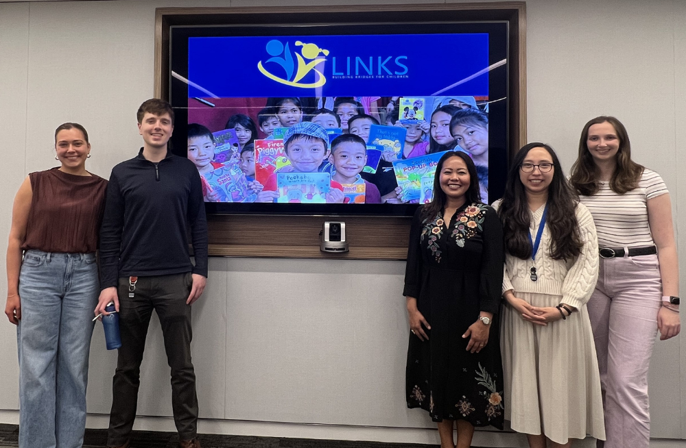 A group of men and women smiling at the camera. They are standing around a screen that says "LINKS" and has a picture of smiling children.
