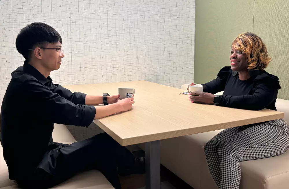 A smiling man and woman sit across from each other at a table. They are each holding coffee mugs.