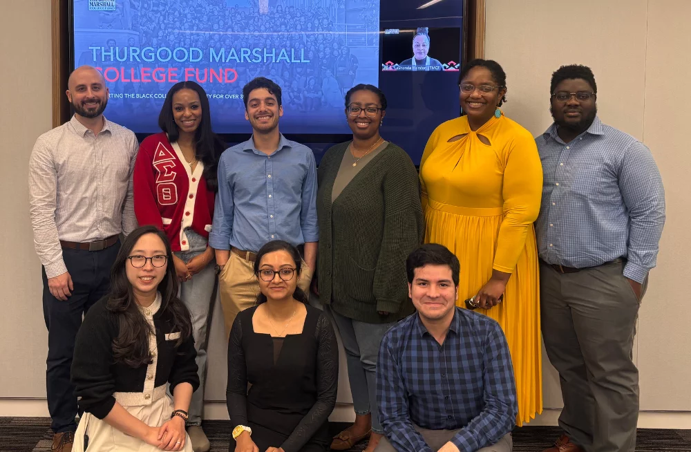 A group of men and women are gathered together and smiling at the camera. The front row is seated while the back row is standing. A screen behind them is titled “Thurgood Marshall College Fund.”