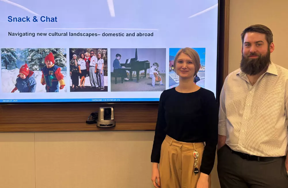 A smiling young man and woman stand next to a screen titled “Snack & Chat: Navigating new cultural landscapes—domestic and abroad.”