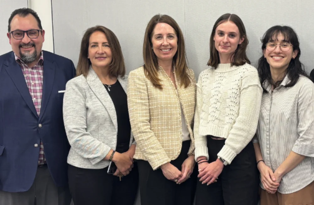 Two younger and three older adults—both men and women—stand together smiling at the camera.
