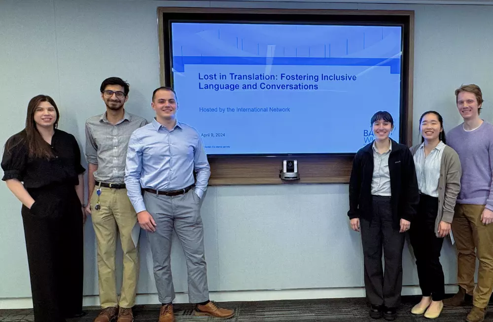 A group of young men and women stand around a screen titled: “Lost in Translation: Fostering Inclusive Language and Conversations.” They are smiling at the camera.